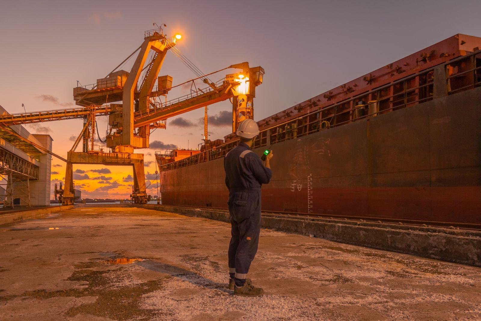 A dock worker in a hard hat beside a berthed vessel at sunset