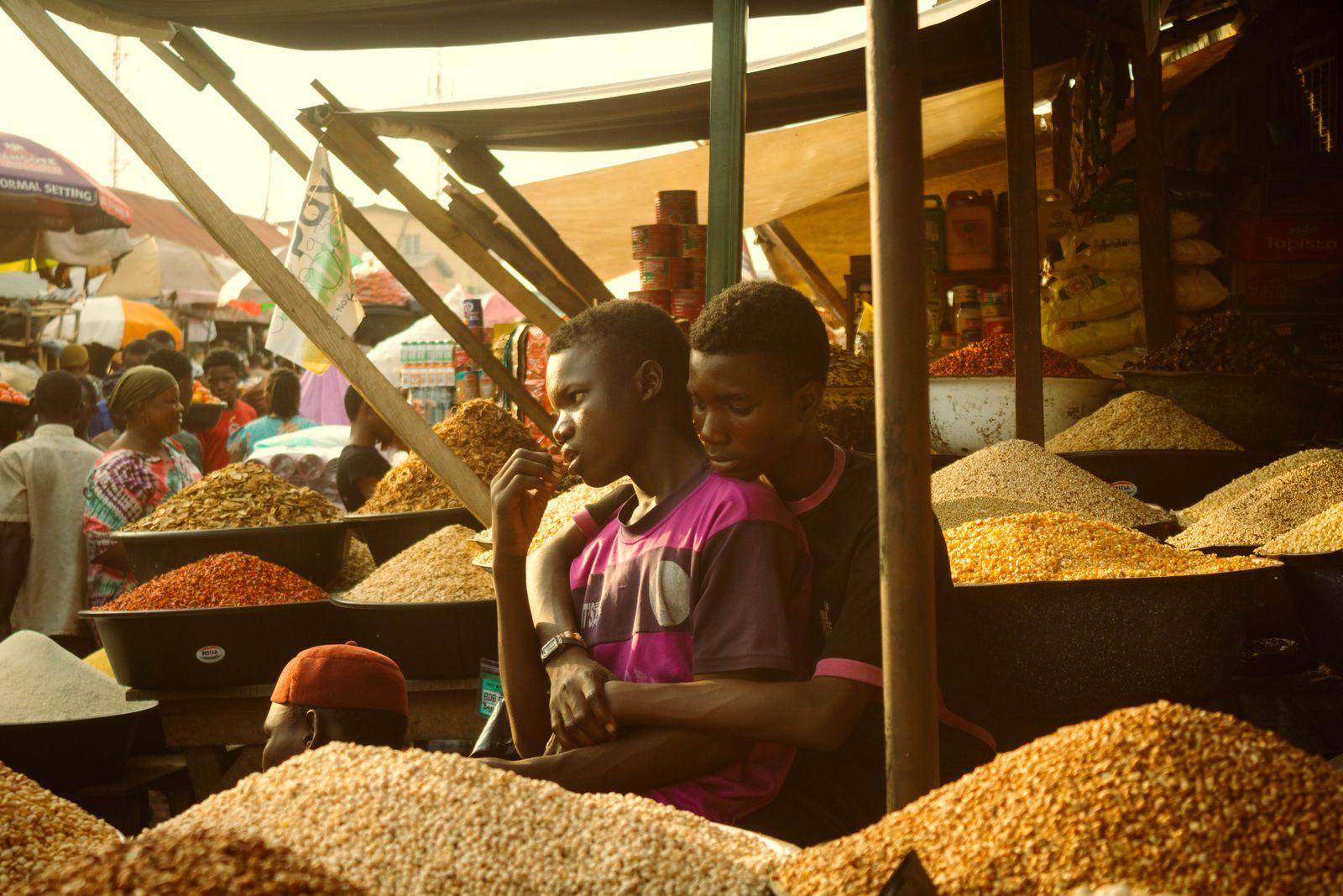 Two traders at a market stall behind heaped sacks of grain, chilli and dried fish